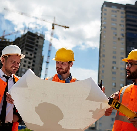Profesionales con casco analizando planos en obra en la Especialización en Gerencia de Empresas Constructoras de la Universidad de América